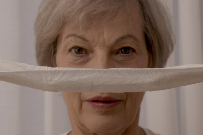 older woman holding an incontinence pad in front of her face