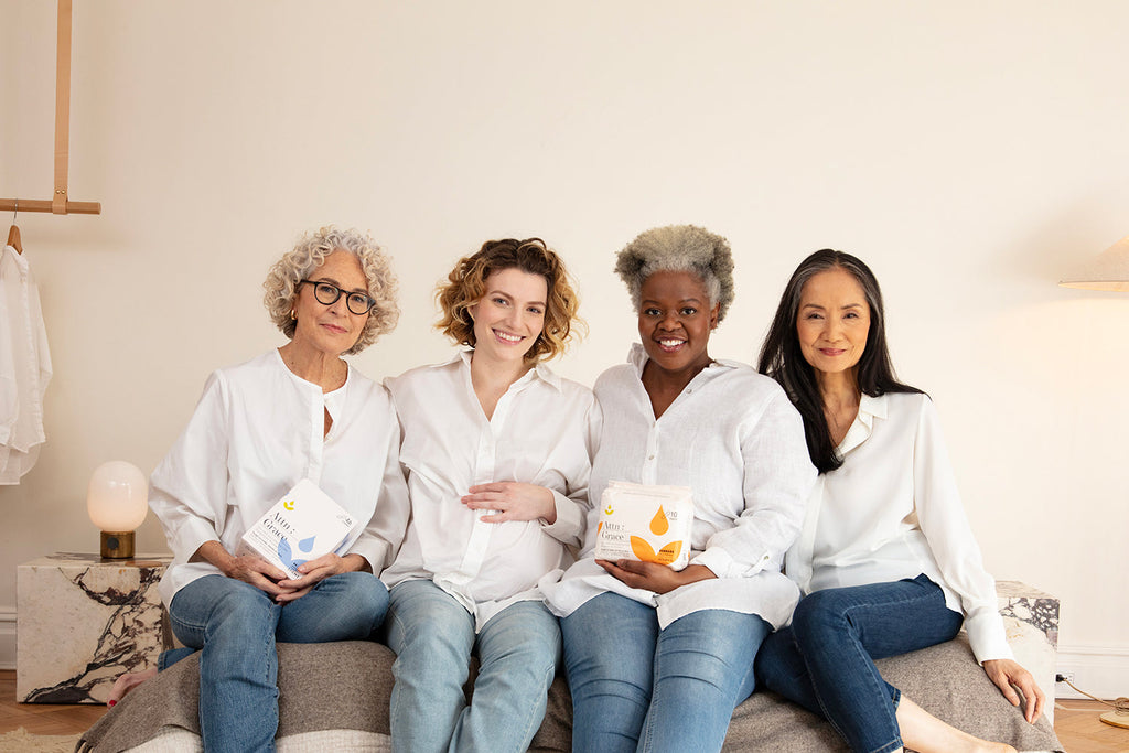 Women sitting next to each other on a bed holding Attn: Grace bladder lea pads