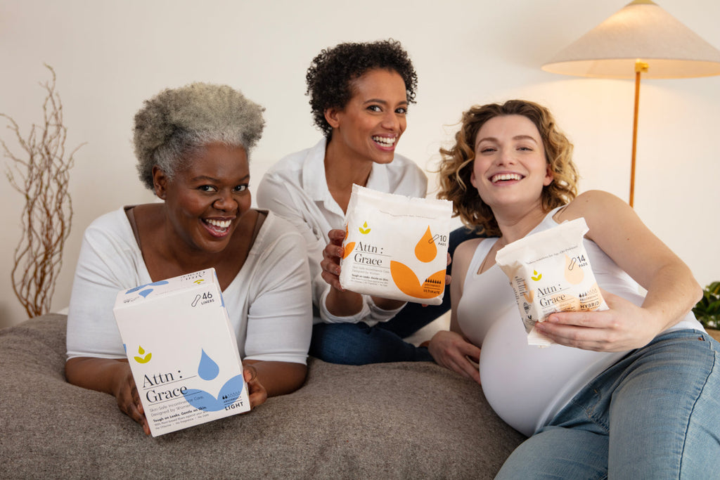 three women sitting on a bed holding up Attn: Grace bladder leak pads and liners