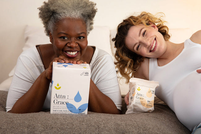 two women on a bed holding packs of Attn: Grace incontinence pads