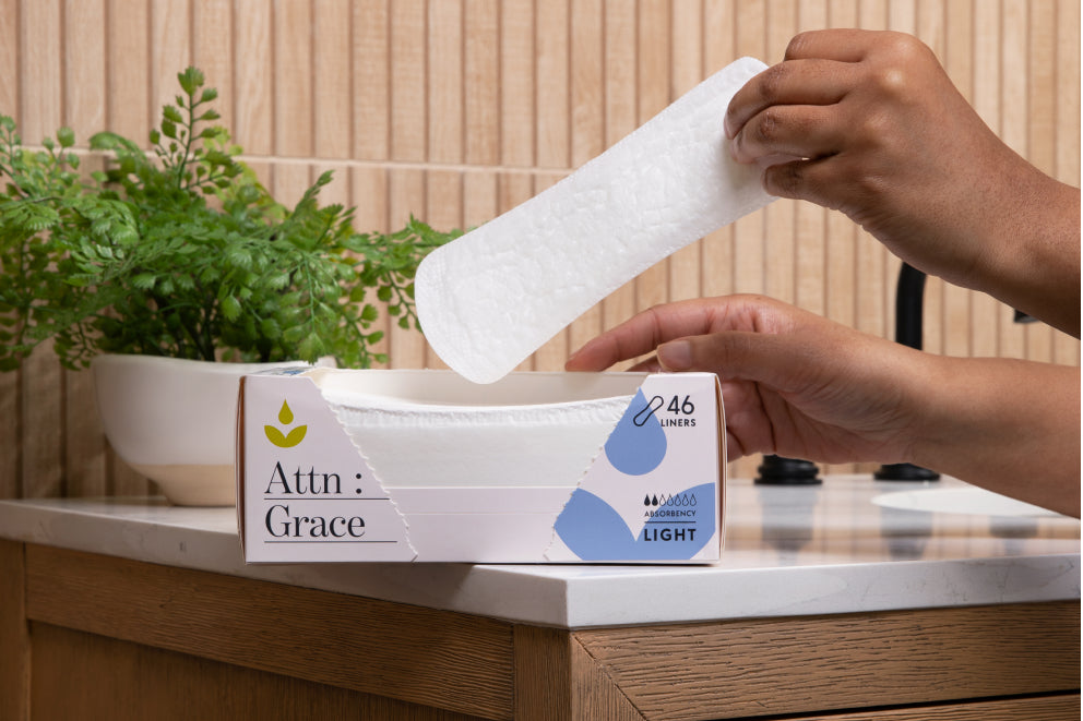 Woman's hands pulling Attn: Grace incontinence liners out of the box