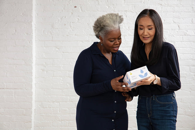 two women standing next to each other holding a box of liners and dicussing them