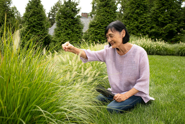 older woman sitting in the grass admiring plants