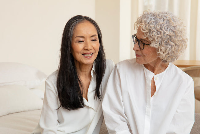 two older women sitting next to each other on the edge of a bed